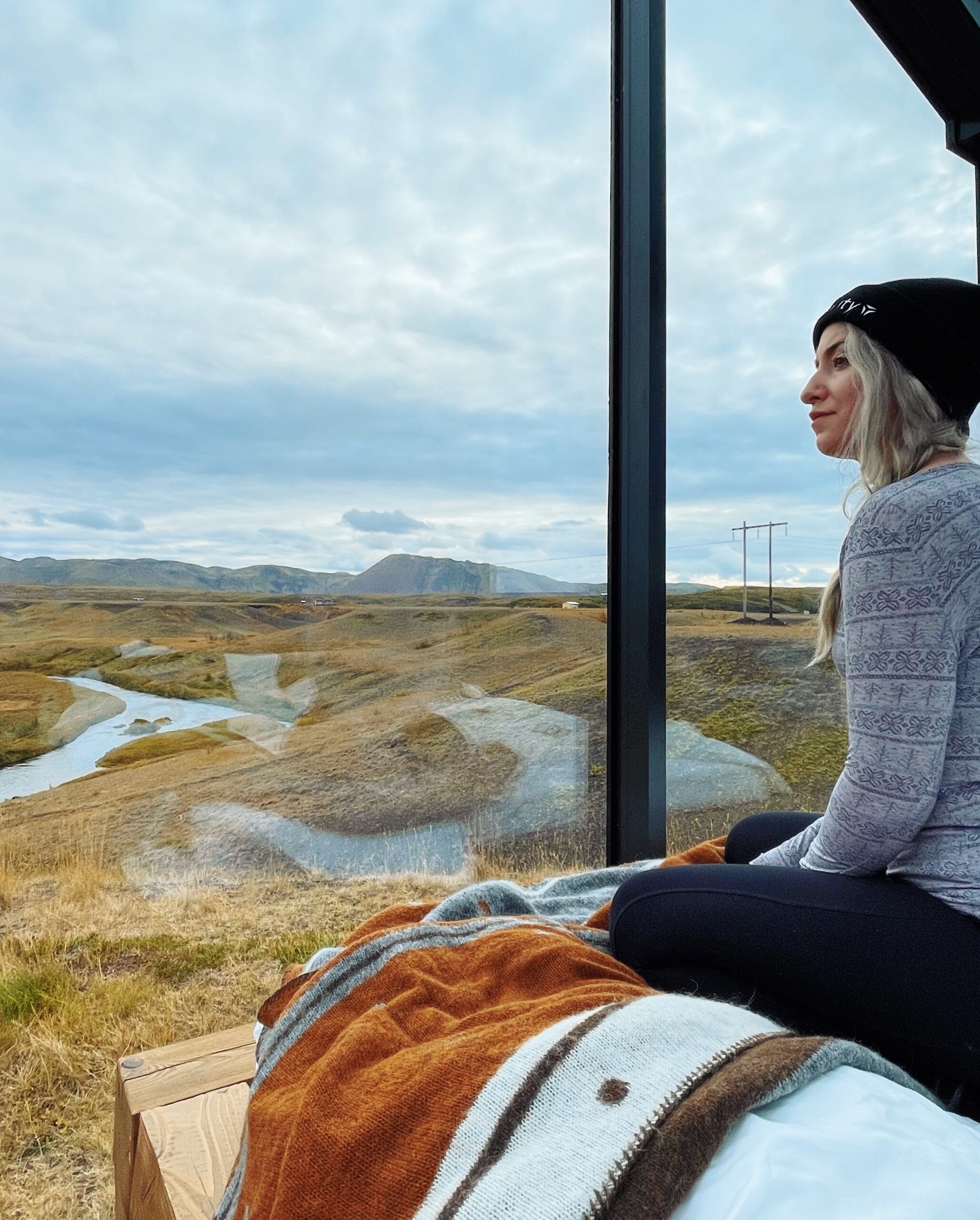 Sitting inside the glass roof cabin on the bed looking out at the Iceland landscape.