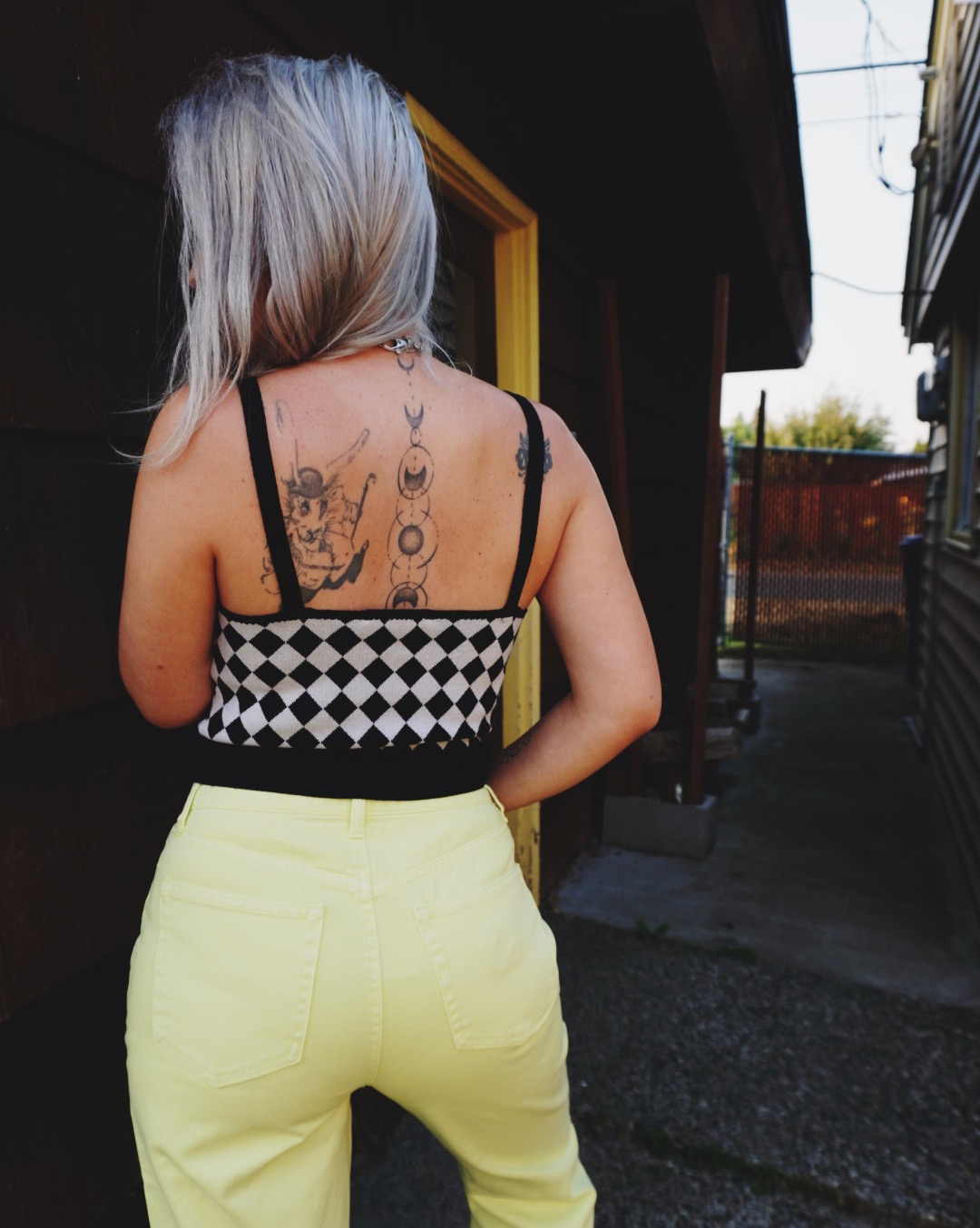 The back of a woman wearing a black and white checkered tank top and neon yellow jeans