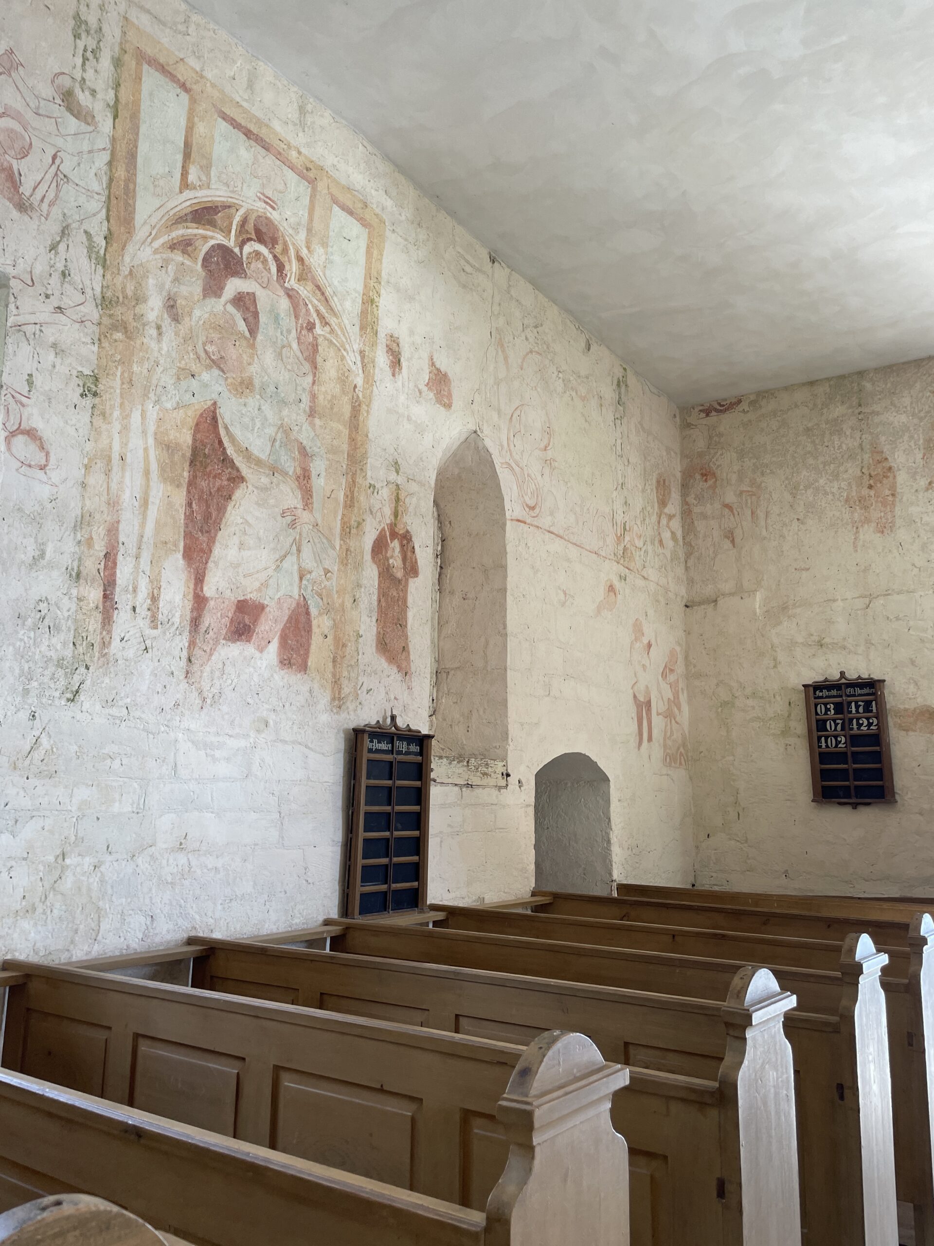 The interior of Højerup old church in Stevns Klint Denmark. There are old faded religious imagery on the walls that look medieval. 